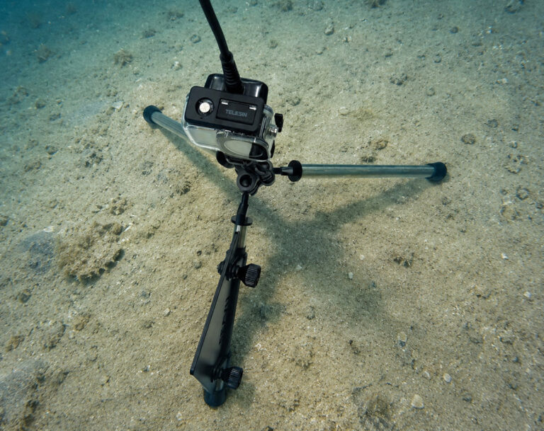 Seavu Seeker Seafloor Stand tripod set up on the sandy seabed with an action camera mounted, cable running to the surface