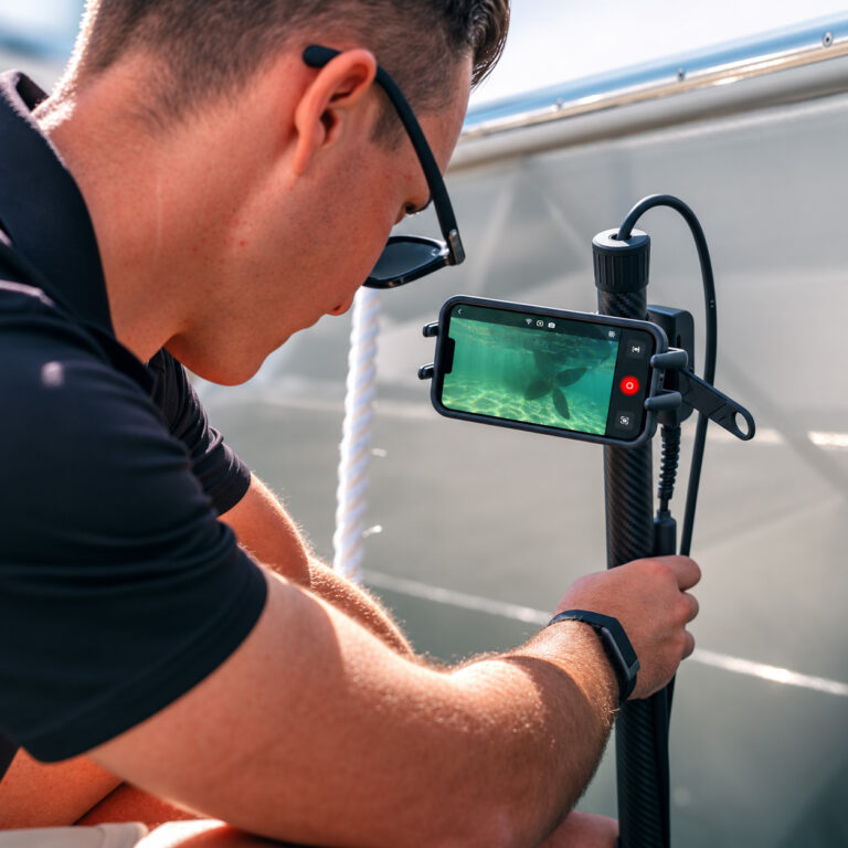 Live underwater view from the Seavu Seeker Pole Kit shown on a phone mounted to the carbon-fibre pole — a technician watches and records real-time footage during a hull inspection