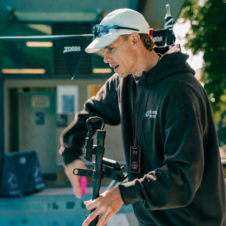 Swim coach poolside wearing the Seavu Swim Coaching Audio System transmitter and holding a Seavu Seeker camera pole