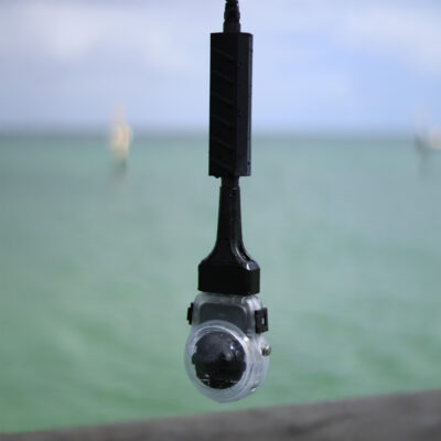 Seavu Orbit 360 Drop Rig with DJI Osmo 360 hanging from its cable over green coastal water, ready to lower from a jetty